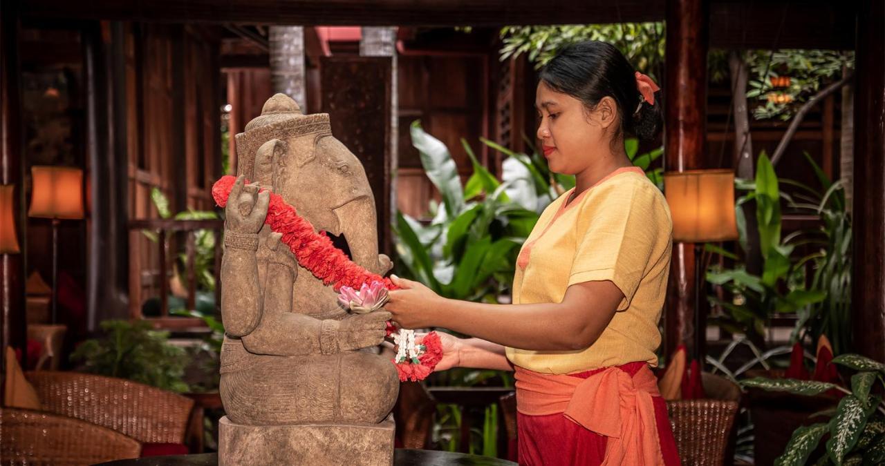 Angkor Village Hotel - Small Luxury Hotels Of The World Siem Reap Bagian luar foto A woman in Thailand, wearing traditional Thai clothing, garlands a statue of the Hindu god Ganesha.